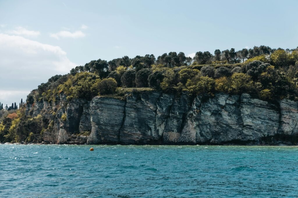 Scogliera rocciosa sul lago con acqua turchese e vegetazione verde.